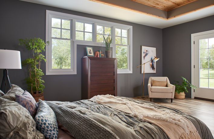 Cozy bedroom of a home with custom double-hung windows and custom picture windows, as well as a hinged patio door within view.
