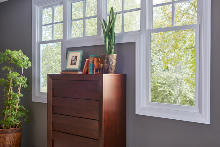 A gray wall in a house with custom double-hung windows around a dresser.