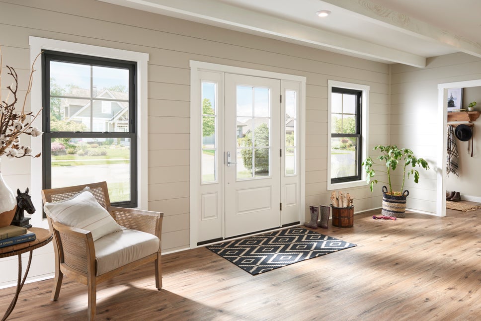 A living room with a white entry door with 2 sidelites and 2 black double-hung windows