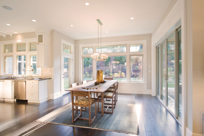 A dining room flooded with natural light from picture windows and patio doors. Window frame material will impact the room’s insulation more than average.