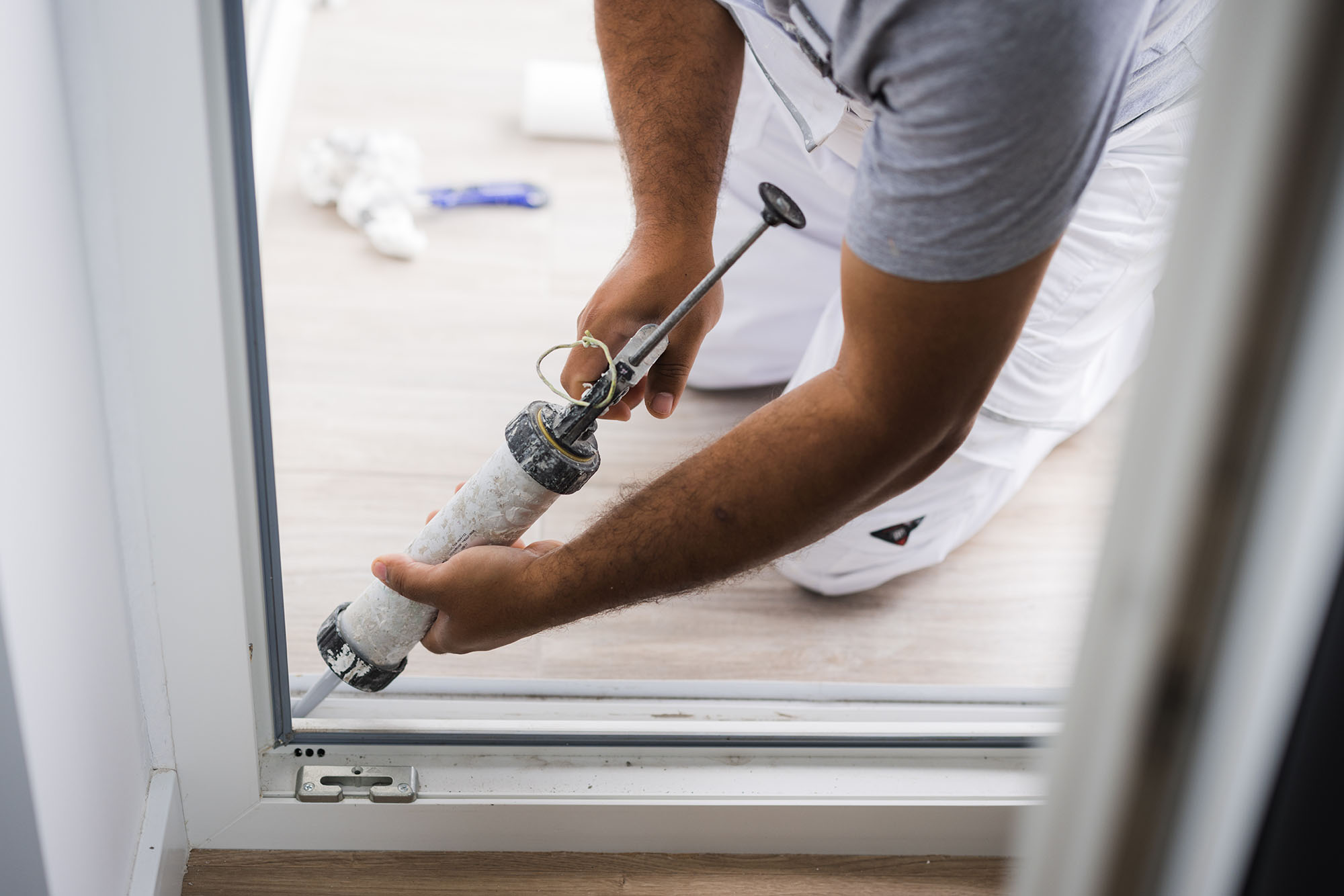 A person applying caulk to a patio door frame.