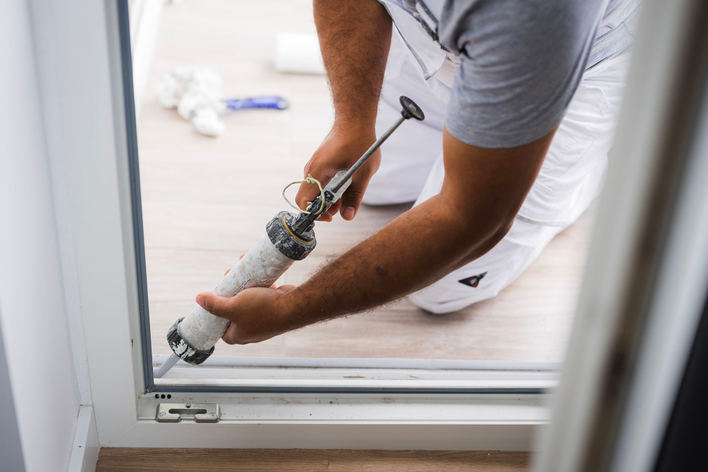 A person applying caulk to a patio door frame.