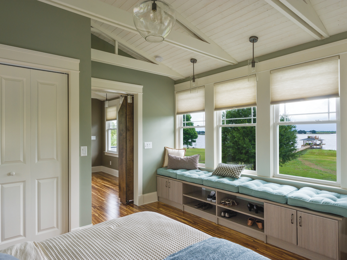 A bedroom with several single-hung vinyl windows overlooking a nearby body of water.