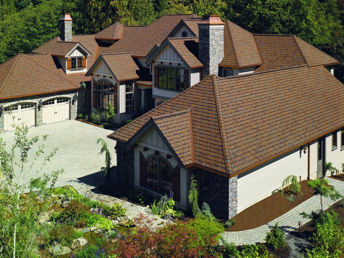 Brown shingles on the hip roof of a home with a large driveway and several architectural-shaped windows.