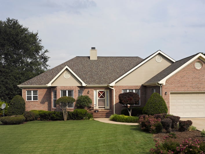 The well-maintained front yard of a brick house with asphalt shingle roofing.