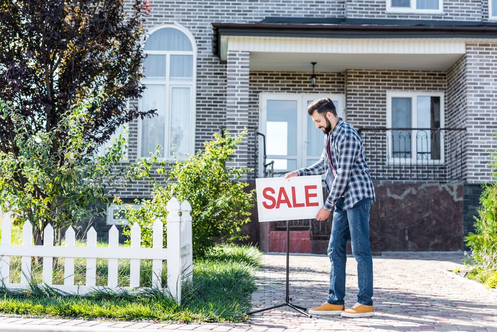 Home Owner Putting Down For Sale Sign in Front of House