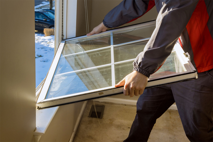 A man winterizing a home by replacing a drafty window.