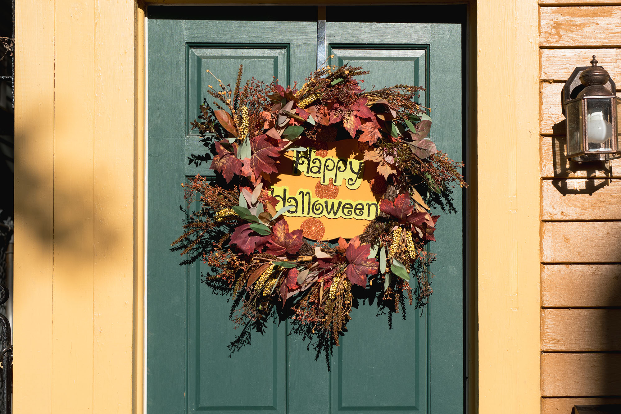 A fall-themed wreath on a green front door of a home that reads “Happy Halloween”.