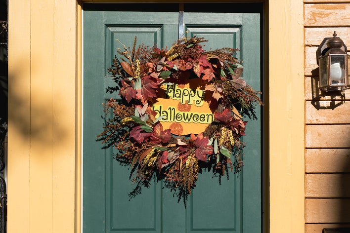 A fall-themed wreath on a green front door of a home that reads “Happy Halloween”.
