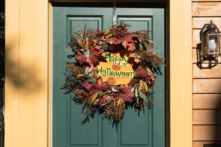 A fall-themed wreath on a green front door of a home that reads “Happy Halloween”.