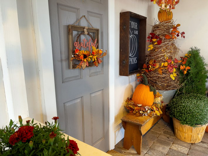 Front door and porch of a home decorated for the Fall season with orange, red, and yellow color patterns.