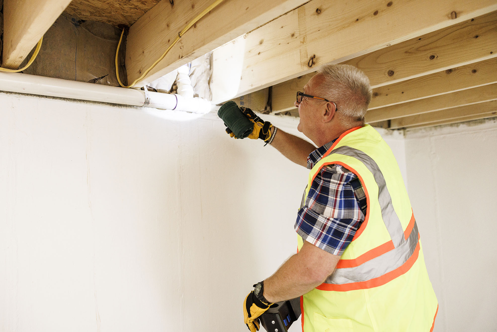 Man conducting a new home inspection using a flashlight to view ceiling insulation.