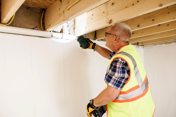 Man conducting a new home inspection using a flashlight to view ceiling insulation.