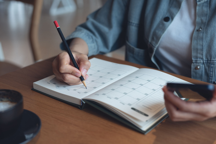 A woman thoughtfully writing in her calendar to set up a professional window installation appointment.