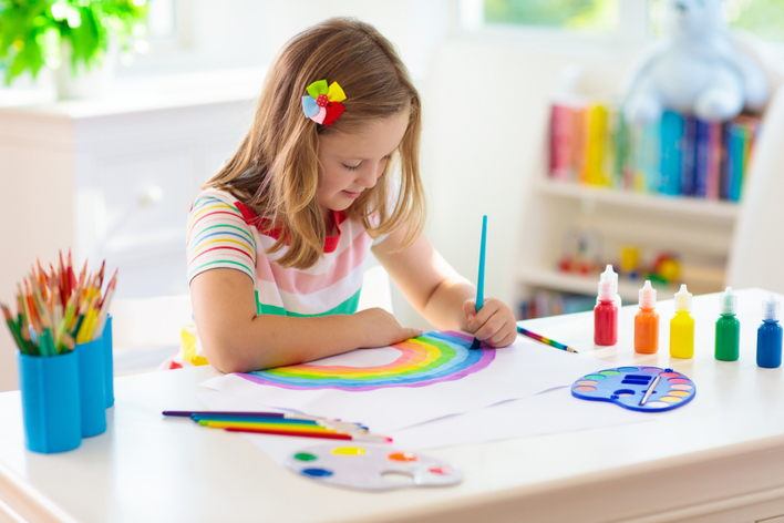 A young girl painting a rainbow in a kid’s craft room