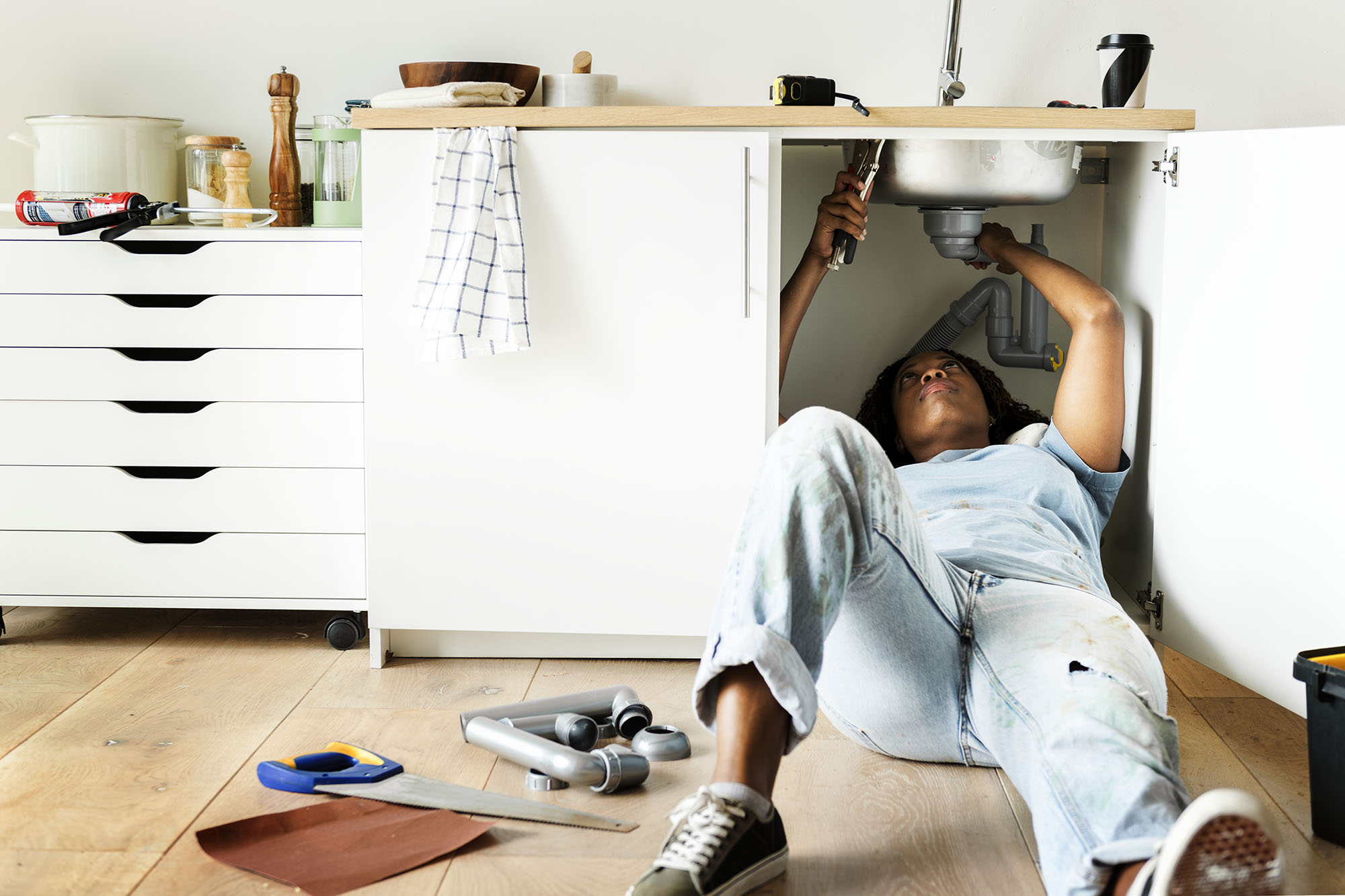 A woman working on the plumbing under a sink as part of DIY home renovations.