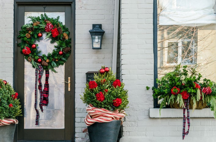 The entryway of a gray-colored house decorated for Christmas, including a wreath hung on the door.