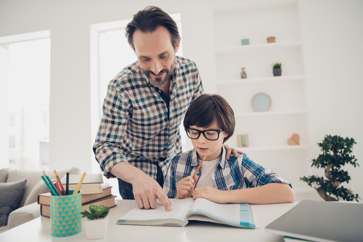 A father helping his young son with homework at the table