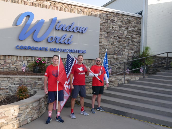 Three men standing in front of Window World Corporate headquarters sign, each holding up a flag — an American flag, a Window World flag, and a Team Red, White & Blue flag.