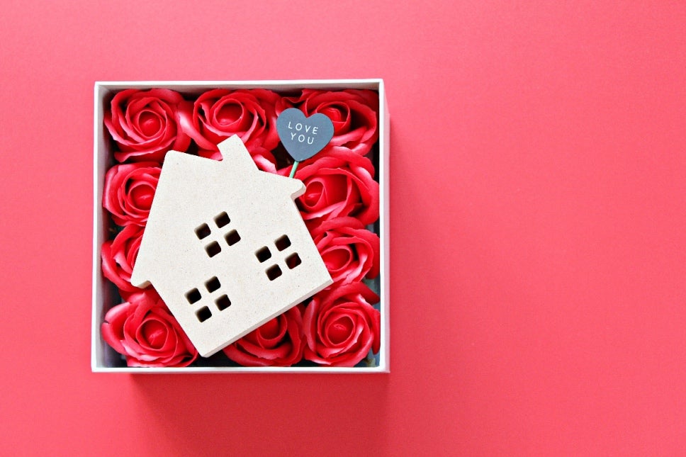 A box of rose petals with a small cutout of a home on top of them