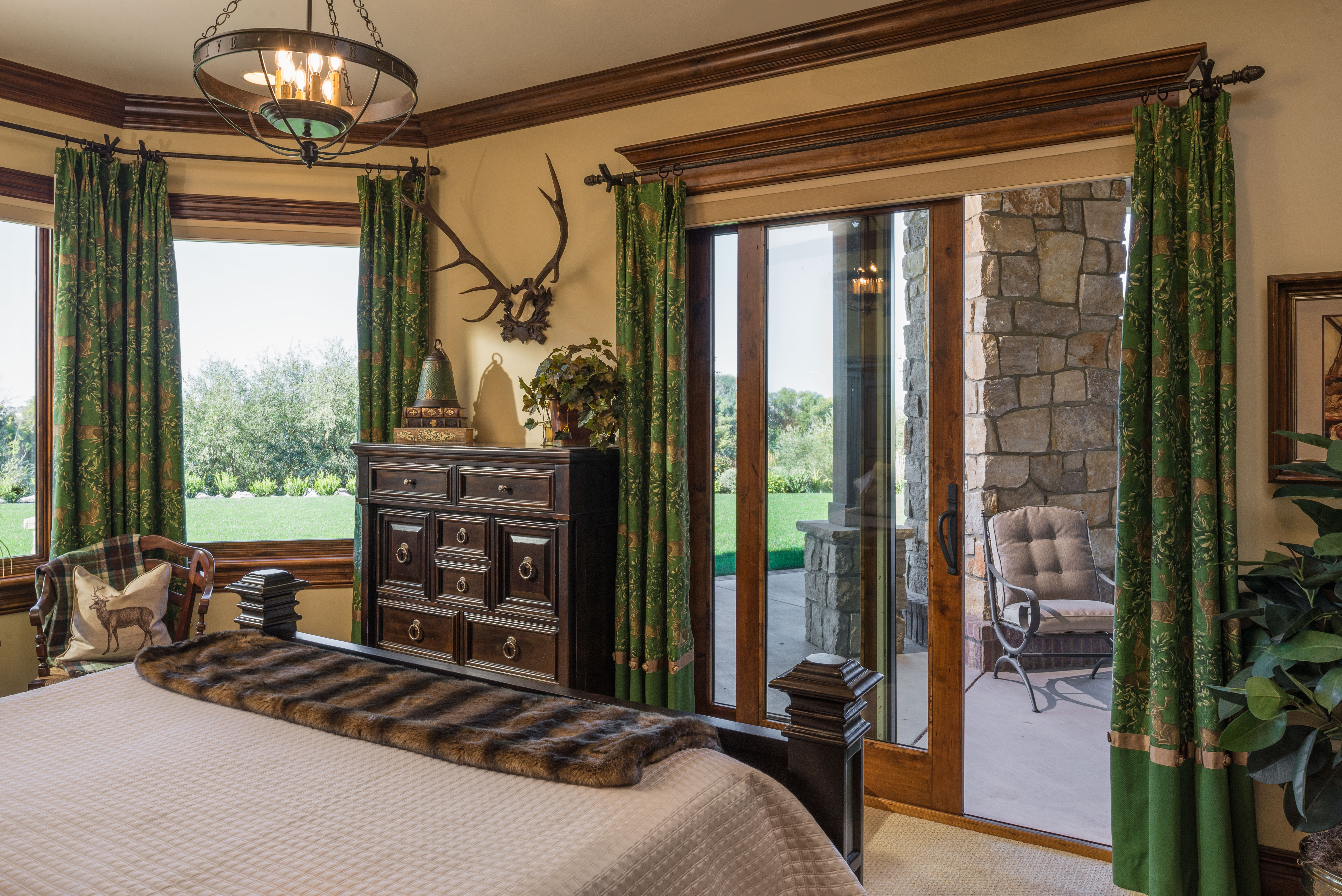 A rustic bedroom with antlers on the wall with a sliding patio door connecting to a covered porch. 