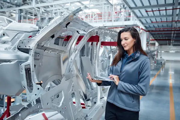 Female maintenance engineer using laptop by car chassis
