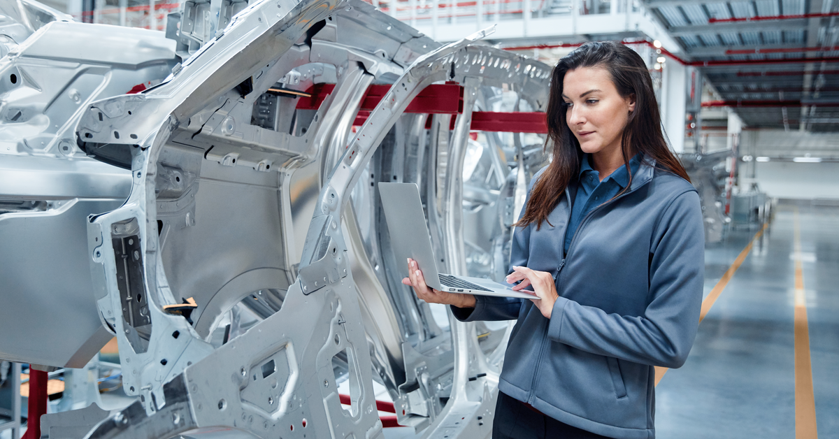 Female maintenance engineer using laptop by car chassis