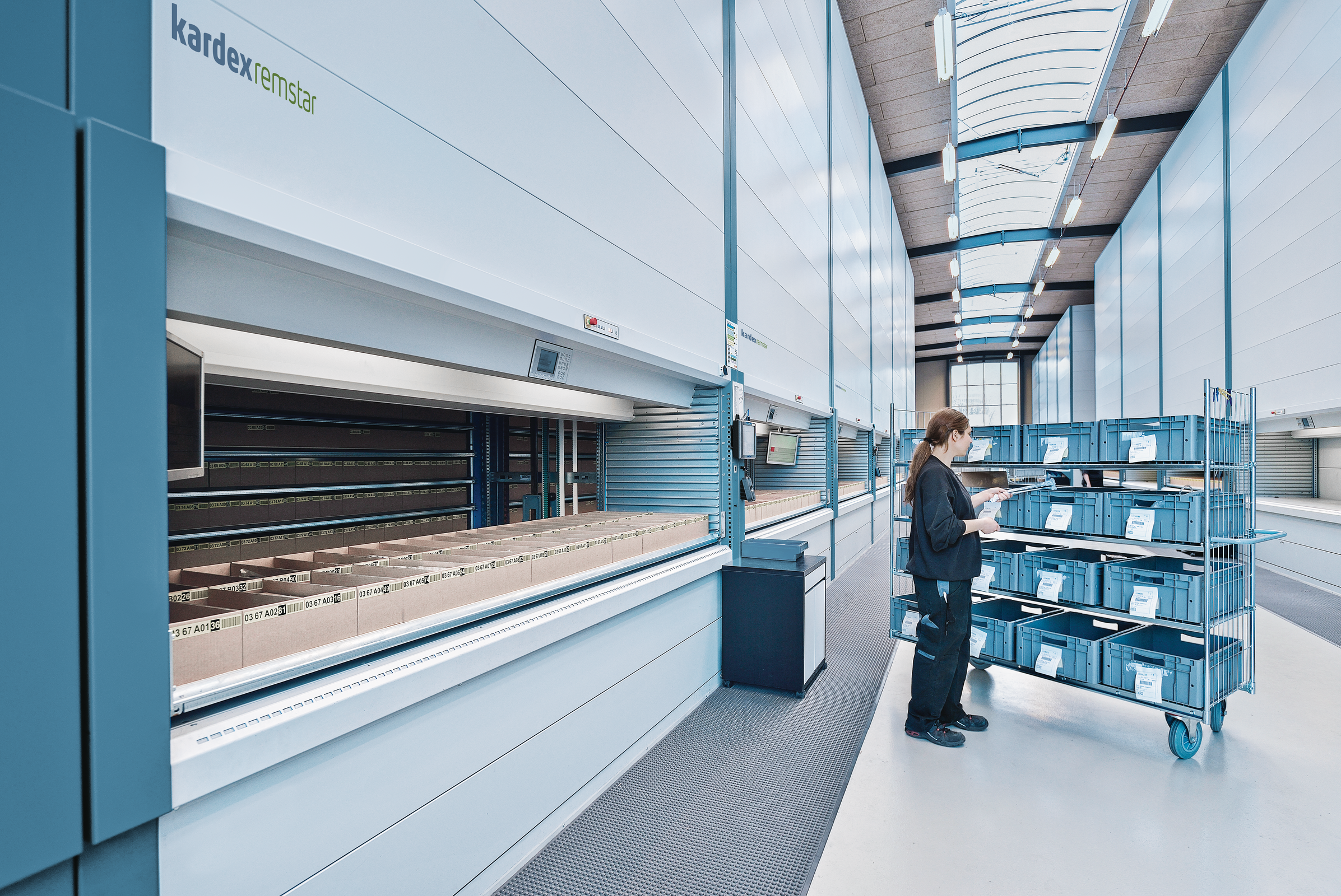 Worker retrieving items from a Kardex Remstar Vertical Lift Module (VLM) in a warehouse, showcasing efficient order picking and vertical storage solutions.
