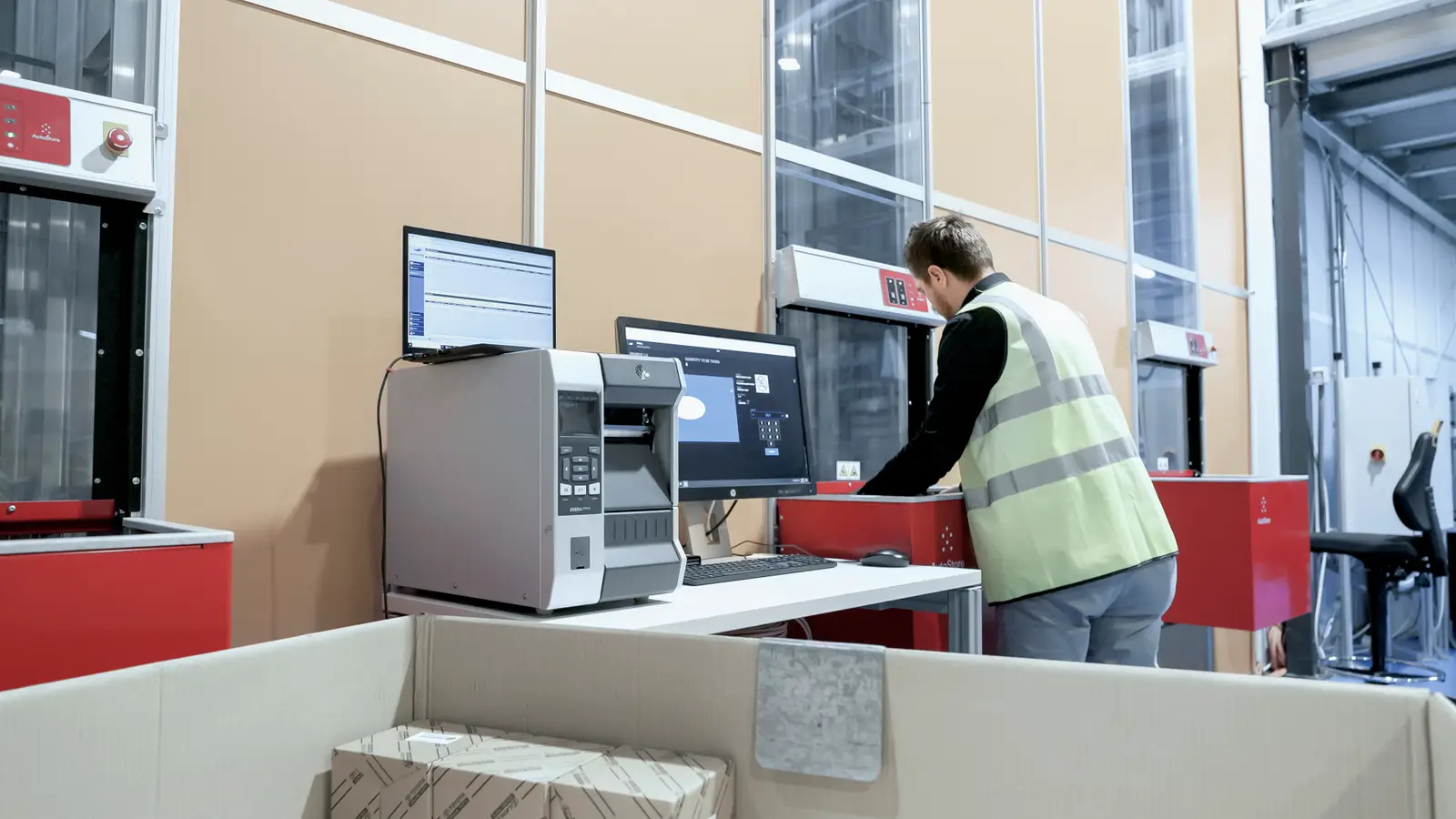 Man in safety vest with hands red AutoStore port next to computer monitor and shipping box
