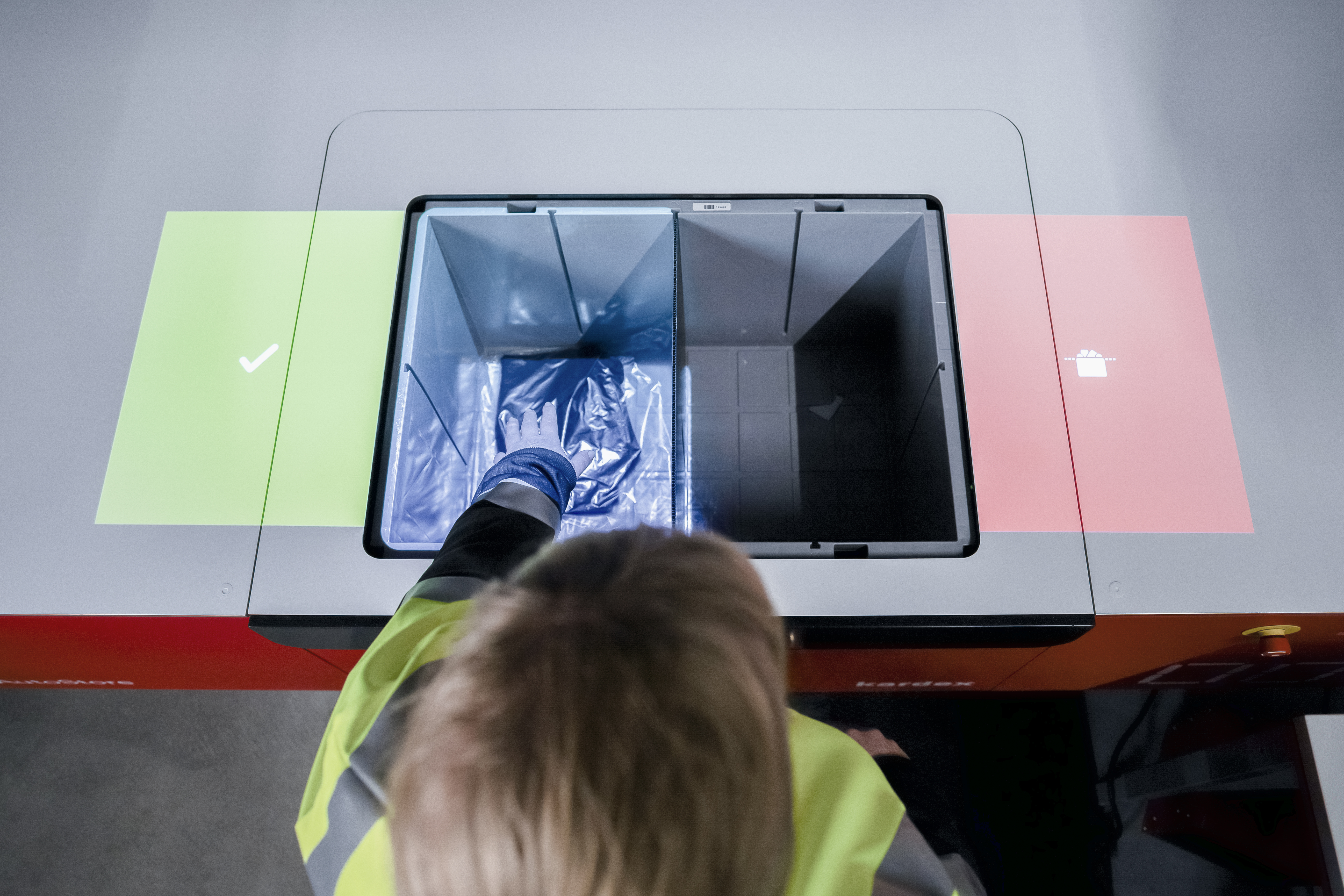Operator placing hand into AutoStore bin with green and red elimumination