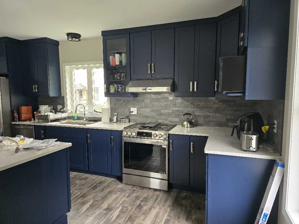 Modern kitchen with navy blue cabinets, stainless steel appliances, and gray backsplash.