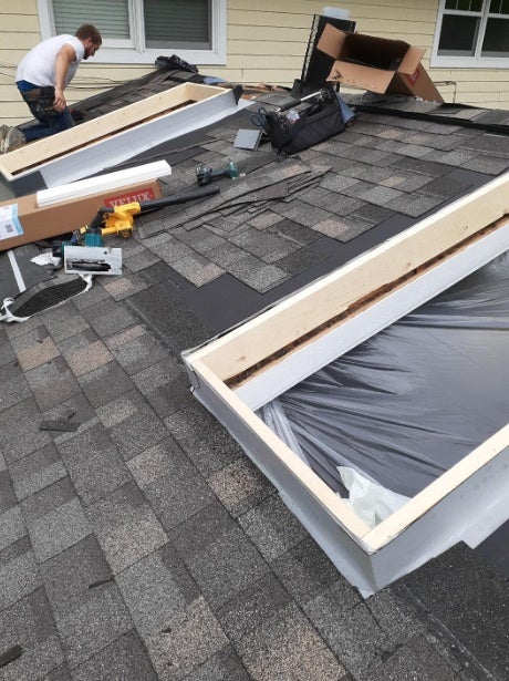 Skylight installation in progress on a shingled roof by expert installers.