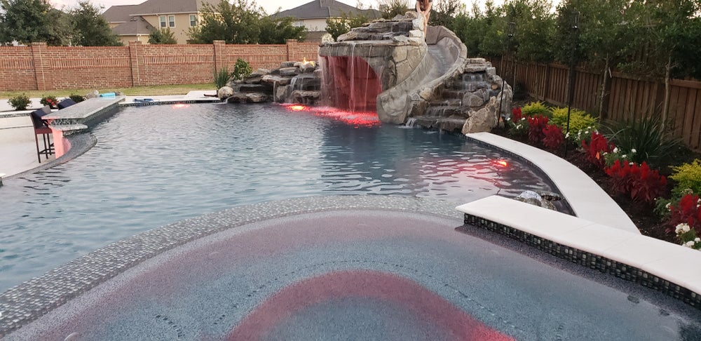 A beautiful inground pool in a Pearland, TX backyard, showcasing a waterfall feature and lush landscaping
