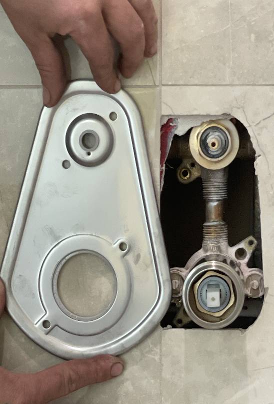 Hands holding a metal plate to adjust a recessed faucet fixture during a plumbing repair service by our honest, family-owned business.