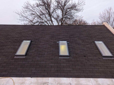 Three newly installed skylights on a shingled roof by professional installers.
