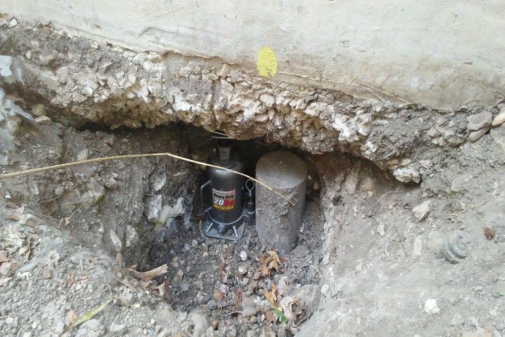 Foundation repair with hydraulic jack and concrete support pier in progress.