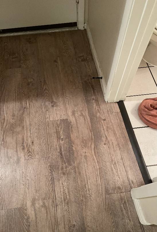 Wooden floorboards near a bathroom entrance showing signs of potential water damage, requiring emergency plumbing inspection and repair