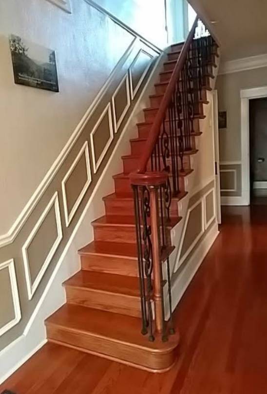 Wooden staircase with iron balusters and wainscoting in residential home