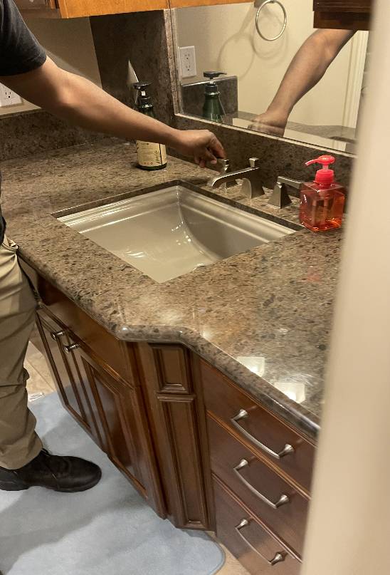 A plumber inspecting a bathroom sink faucet in a residential setting