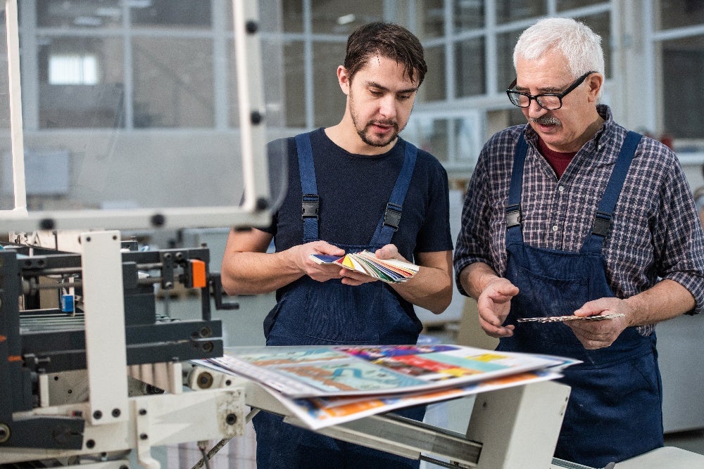 Print shop employees reviewing color swatches and printed samples for quality assurance.