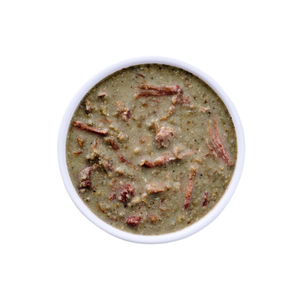 Top view of a white bowl filled with Wild Alaska pollock and pork stew cat food, showing a moist, chunky texture with visible pieces of pork and fish in a light gravy on a clean white background.
