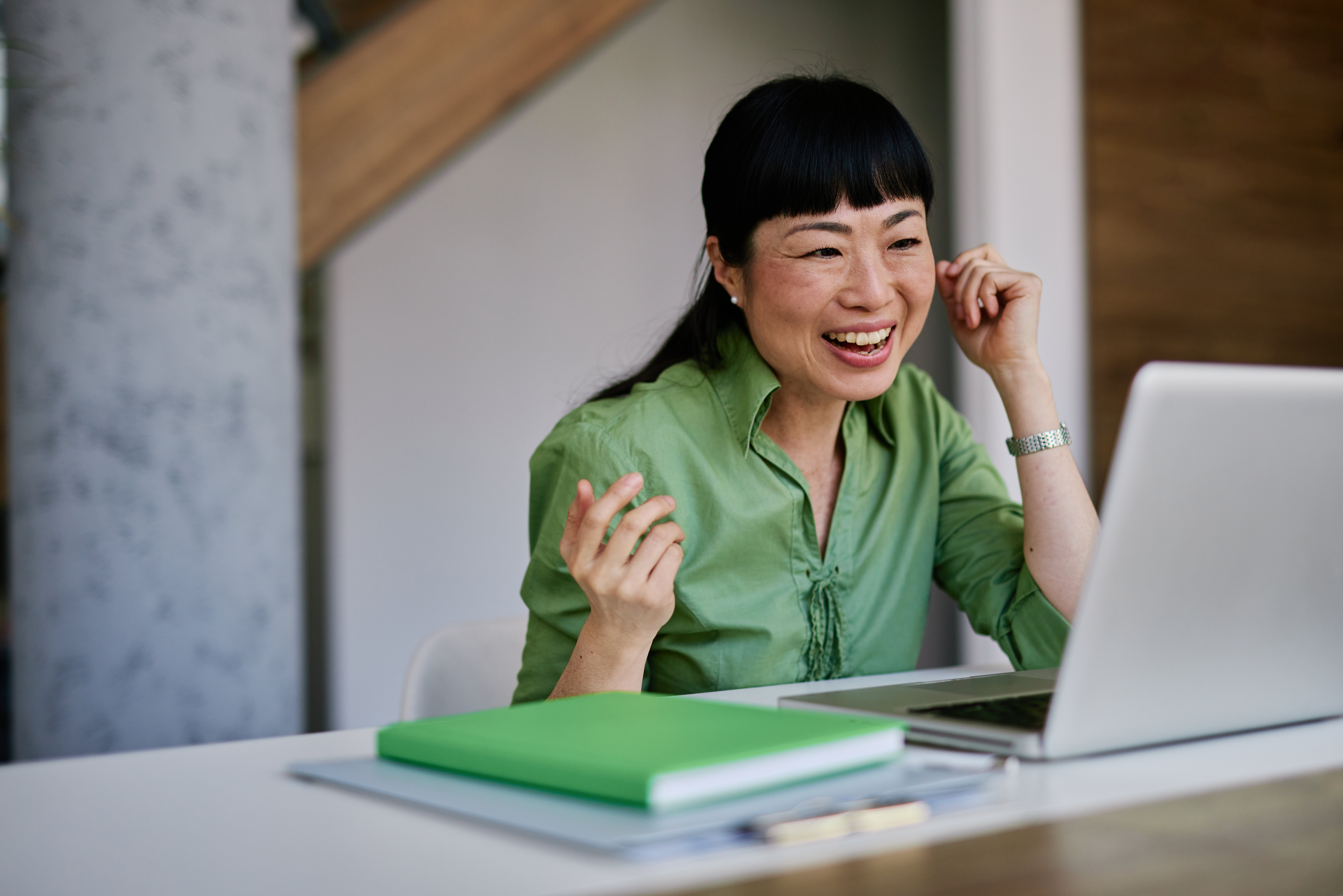 A woman smiles while chatting on her mobile phone and looking at her laptop.