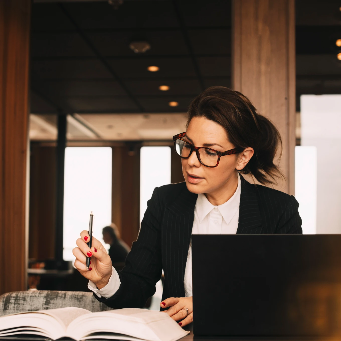 A focused professional refers to a book while sitting in front of an open laptop.
