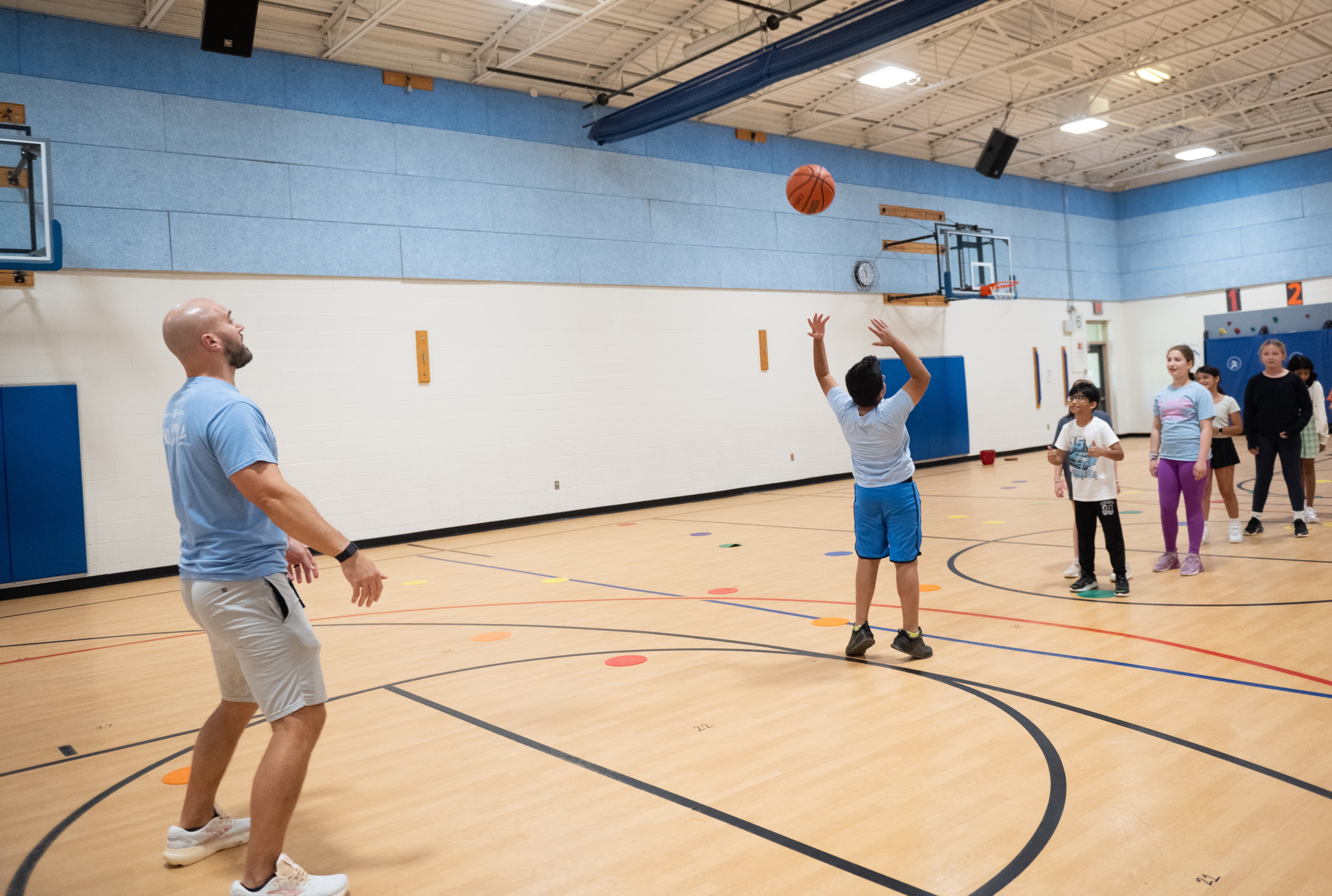 A student attempts an overhead backwards basketball trick while others look on.