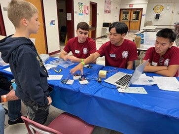 Group of three high school students talking to an elementary student.