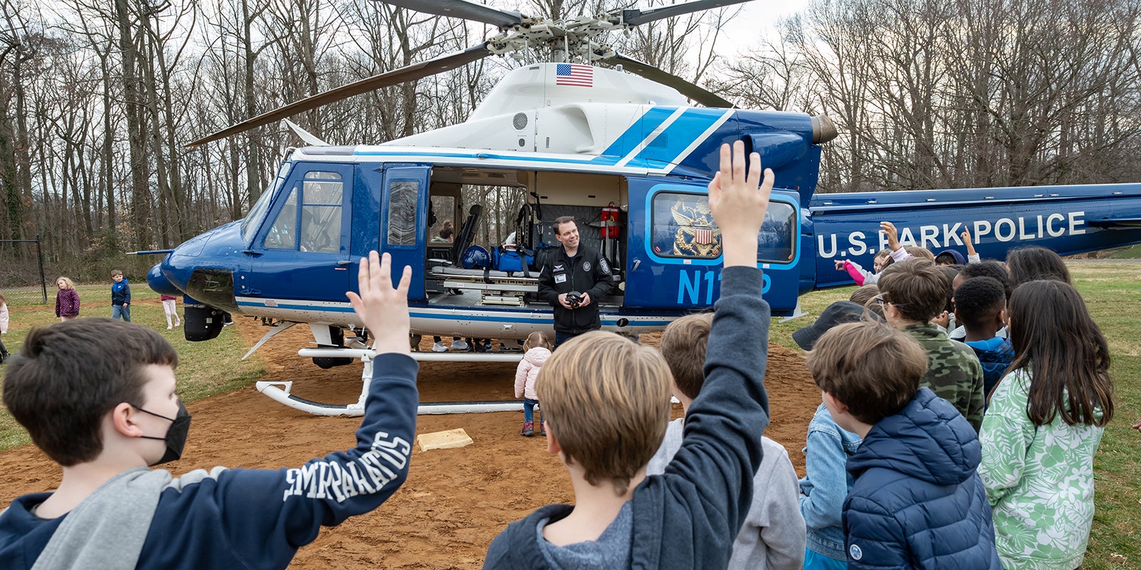 Students raise their hands during a talk with a US Park Police officer in front of his helicopter