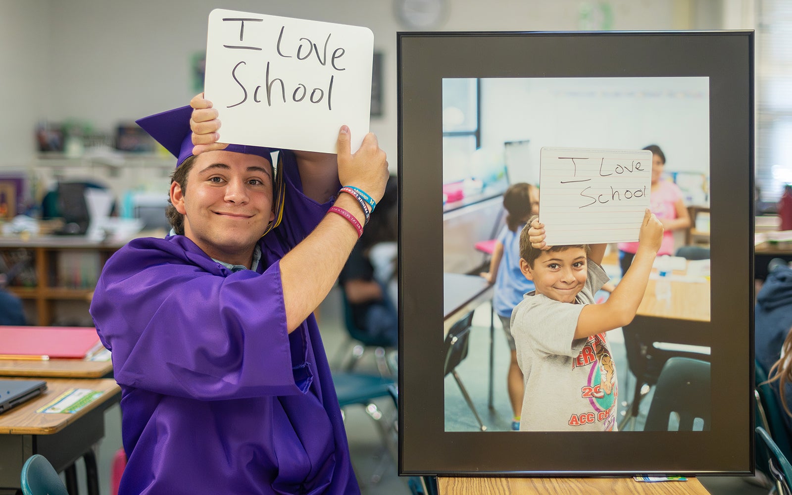 A graduate in regalia holds up a sign saying I love school next to a photo of him as an elementary school student