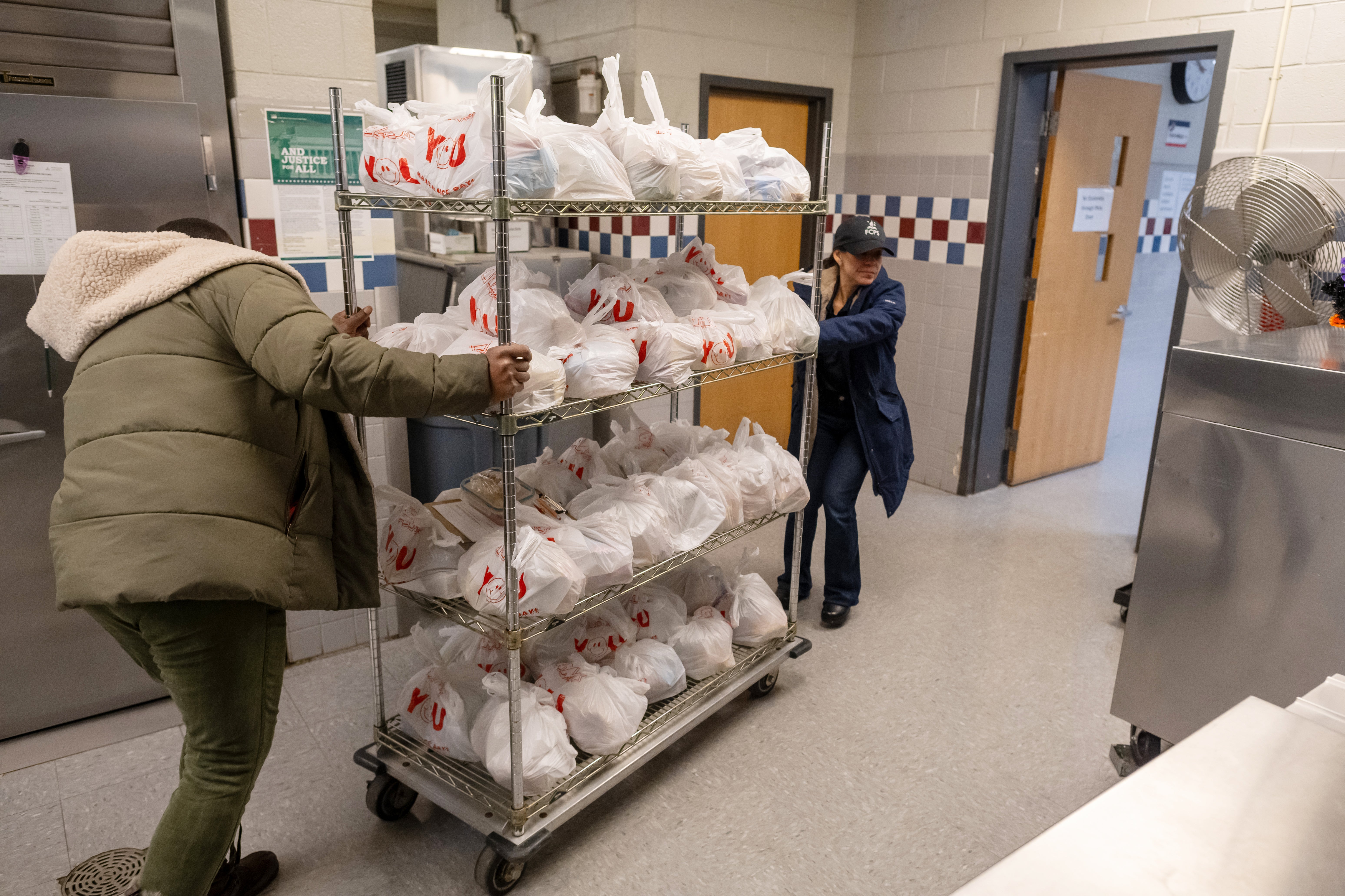 two staff members roll out a cart of completed meal kits