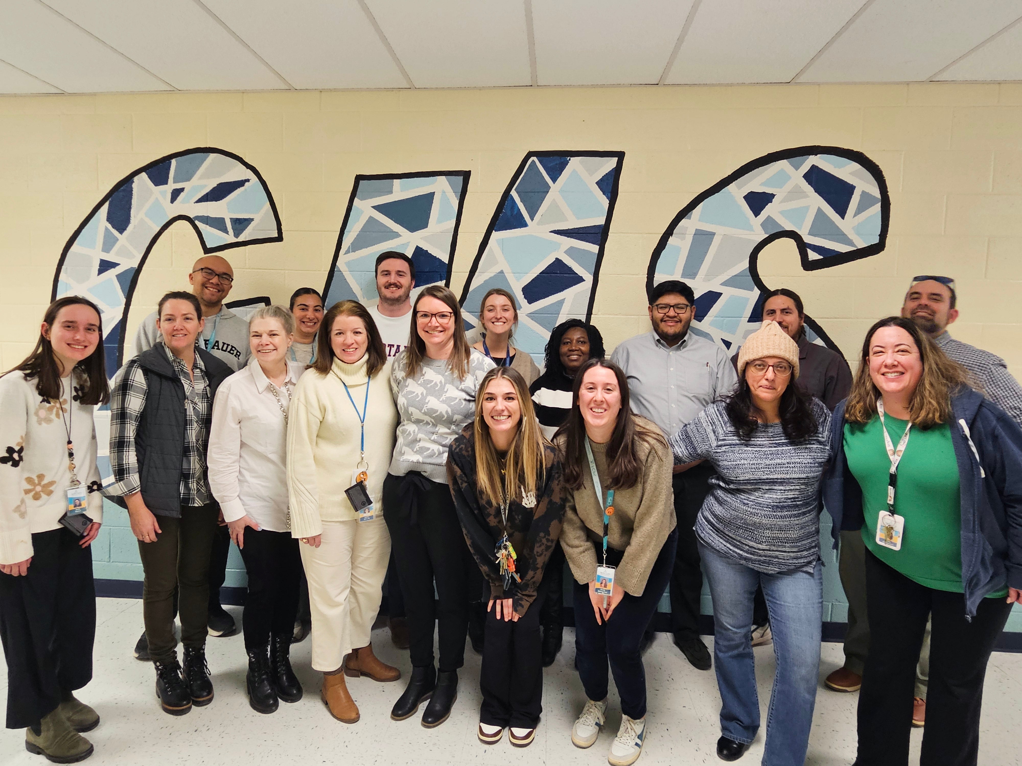 A mix of men and women smile for a group photo in front of three large letters: "GMS," painted in various shades of blue.