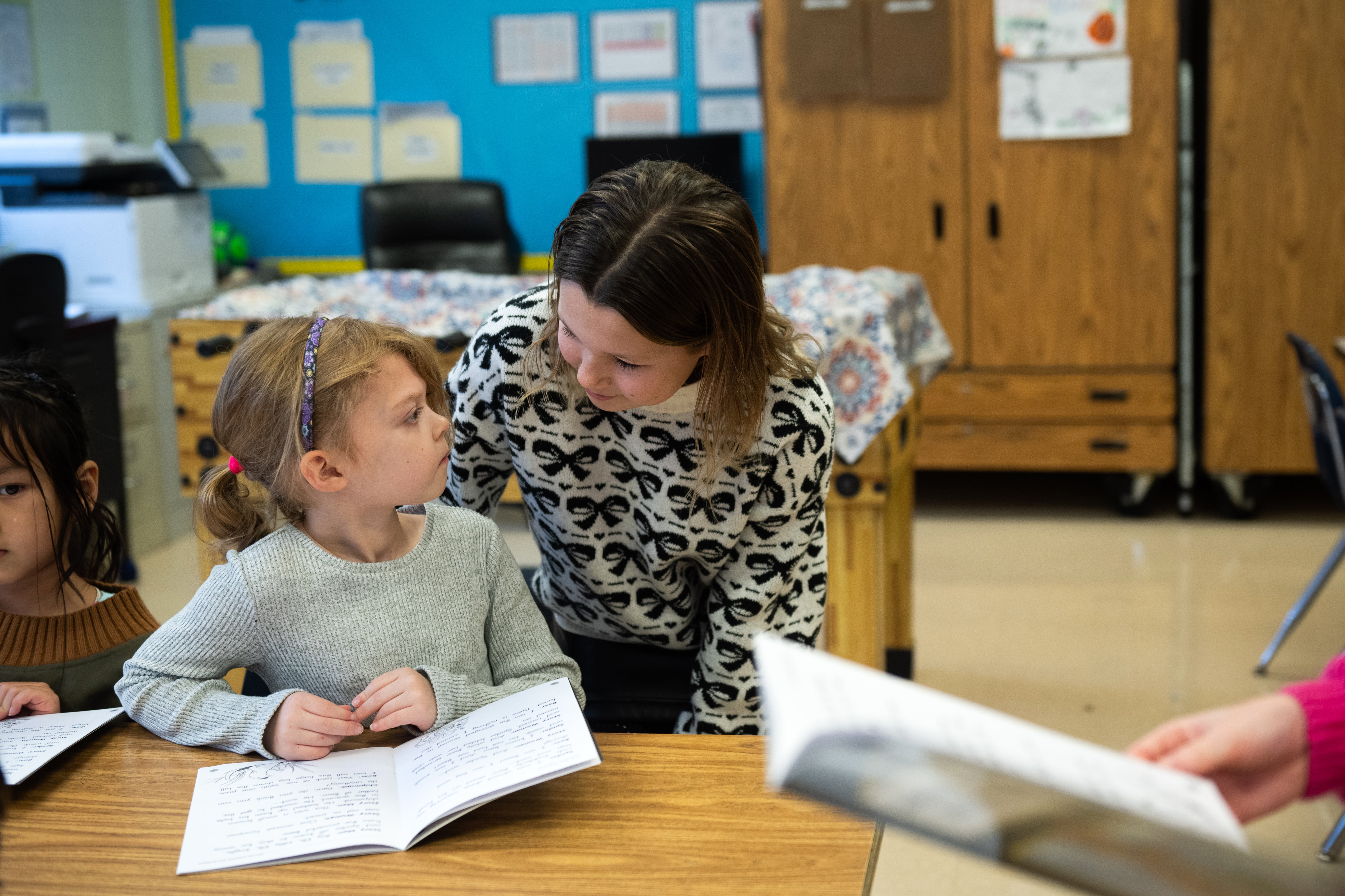 A first grader looks at a sixth grader as they look over a book